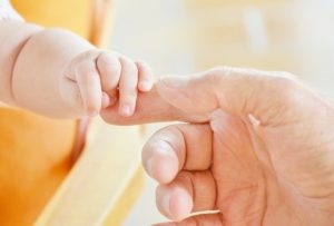 An adult's hand is holding a baby's hand