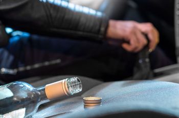 Closeup of an empty alcohol bottle with a drunk driving driver
