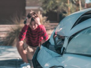 man holding his head while looking at his damaged car