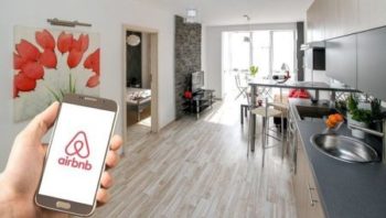 Airbnb app shows on a phone, living room at the background
