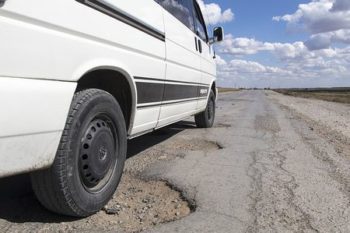 White-color car is driving on a pothole road