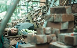 a builder or roofer has fallen from the top elevation of scaffold on a construction site and landed on rubble at the base of the building . He is grimacing in pain