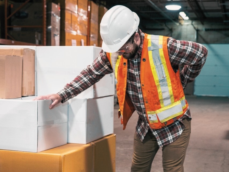 A man experiencing lower back pain at work in a warehouse.