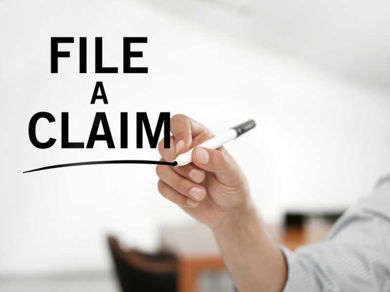 businessman writing "file a claim" on a virtual board 